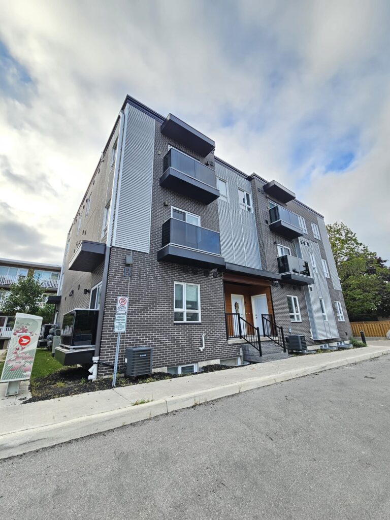 Apartment building with multiple floors and a parking lot in front, featuring several parked cars.