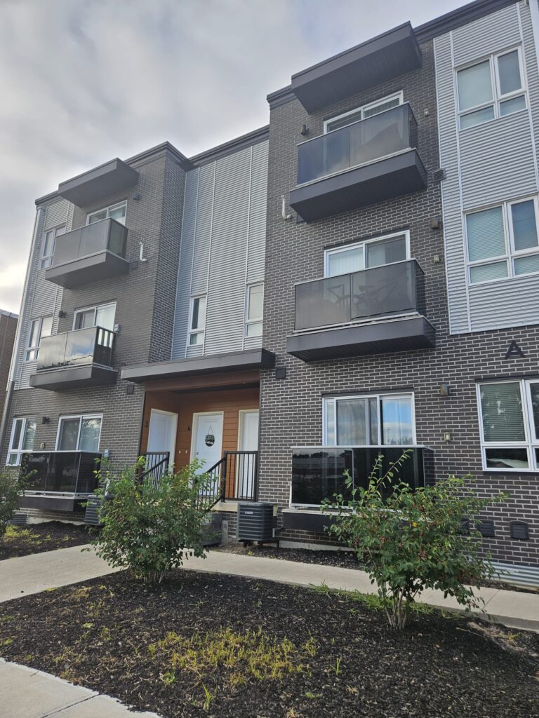 Apartment building with multiple balconies and a sidewalk in front.