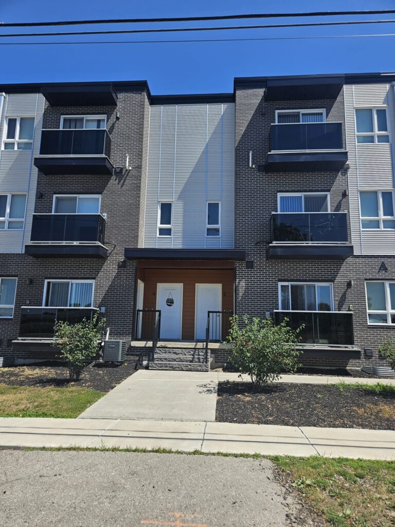 Apartment building with multiple balconies and a sidewalk in front.