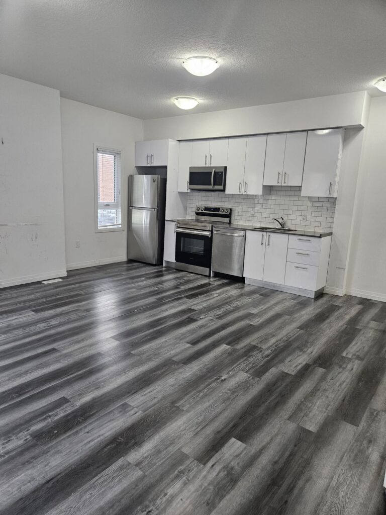 A bright, empty kitchen featuring white cabinets and polished hardwood floors.