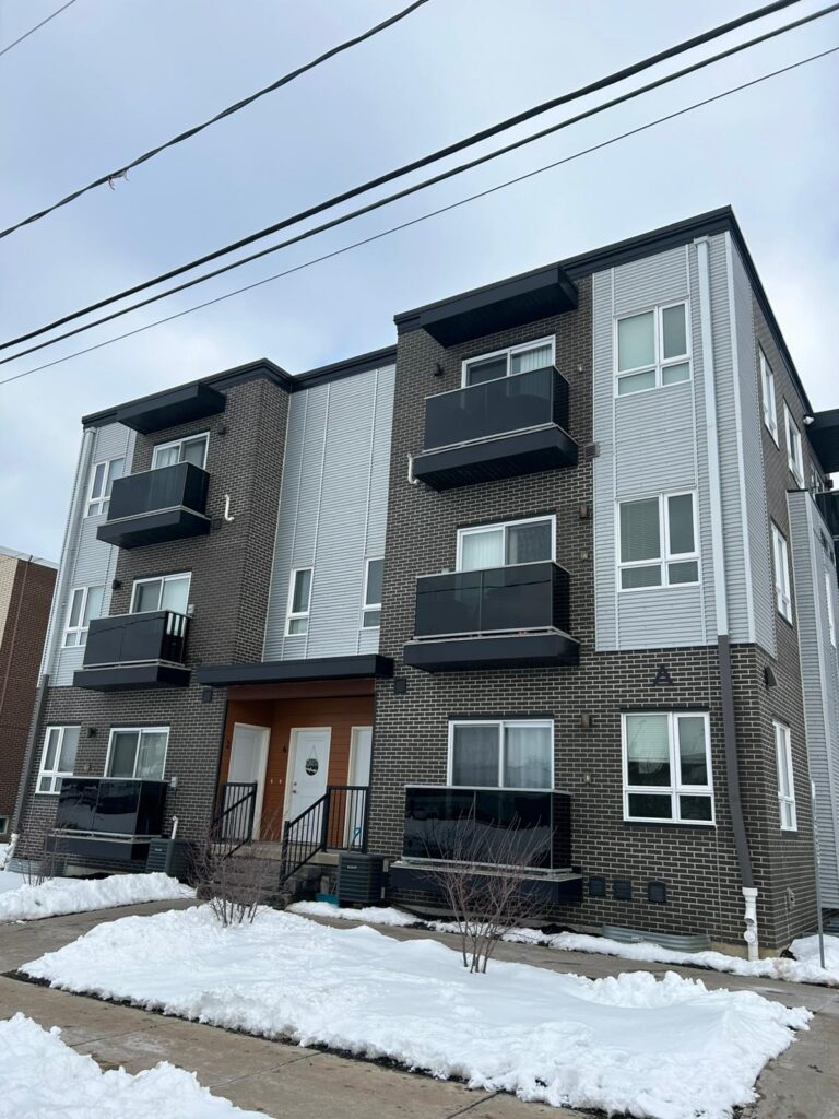 Apartment building covered in snow with a parked car in front on a winter day.