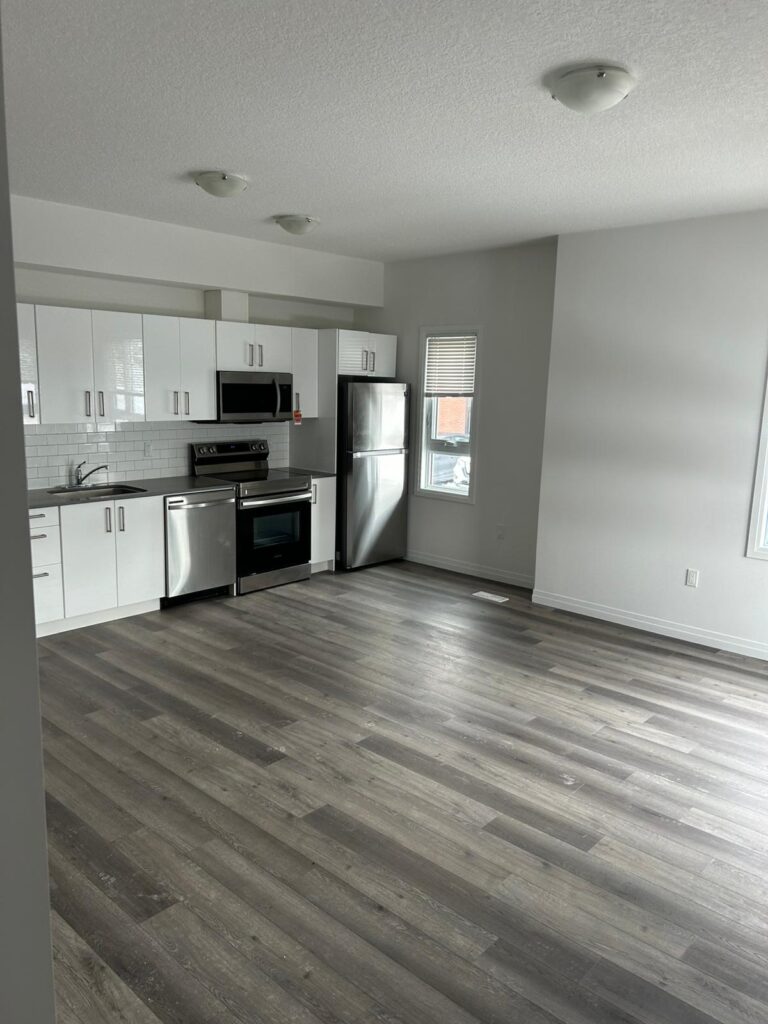 A bright, empty kitchen featuring white cabinets and polished hardwood floors.