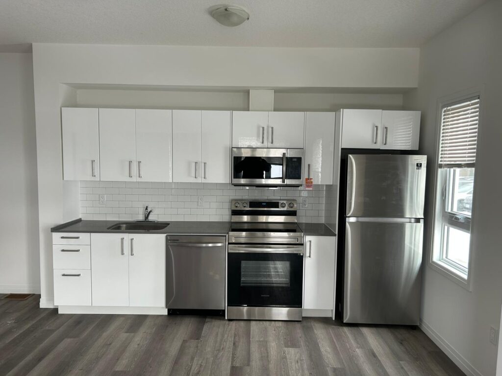 A bright, empty kitchen featuring stainless steel appliances and sleek white cabinets.