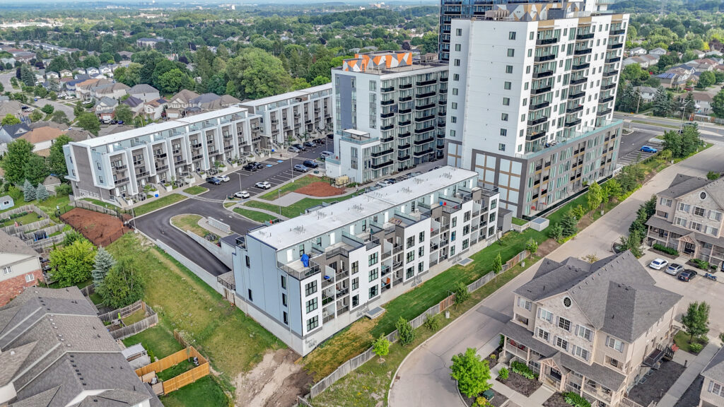 Aerial view of a suburban residential complex with houses, green lawns, and tree-lined streets.