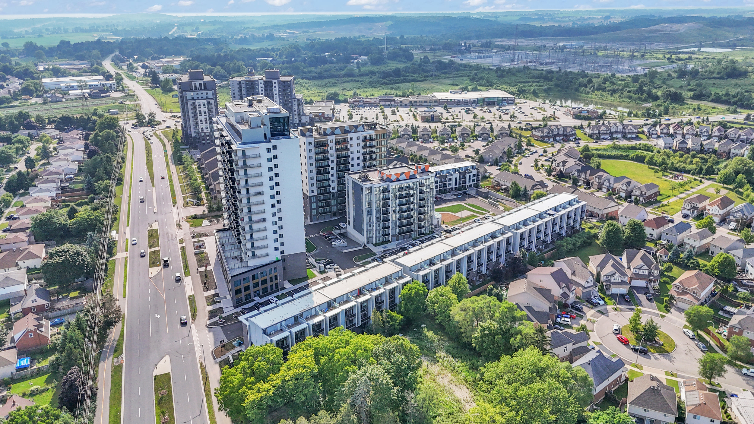 Aerial view of a residential area featuring houses, trees, and a highway running through the landscape.