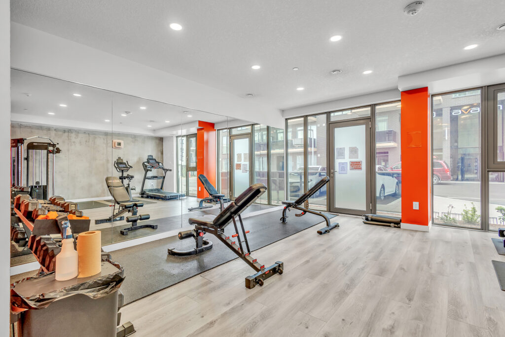 A gym room featuring various exercise equipment and large mirrors on the walls.