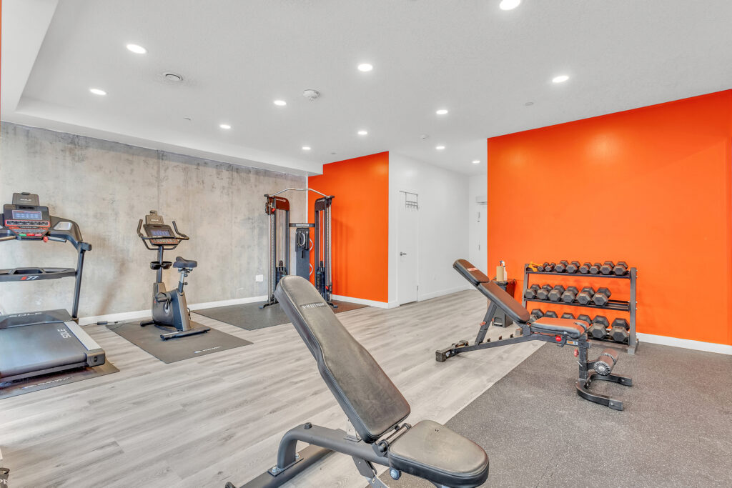A gym room featuring orange walls and various fitness equipment arranged for workouts.