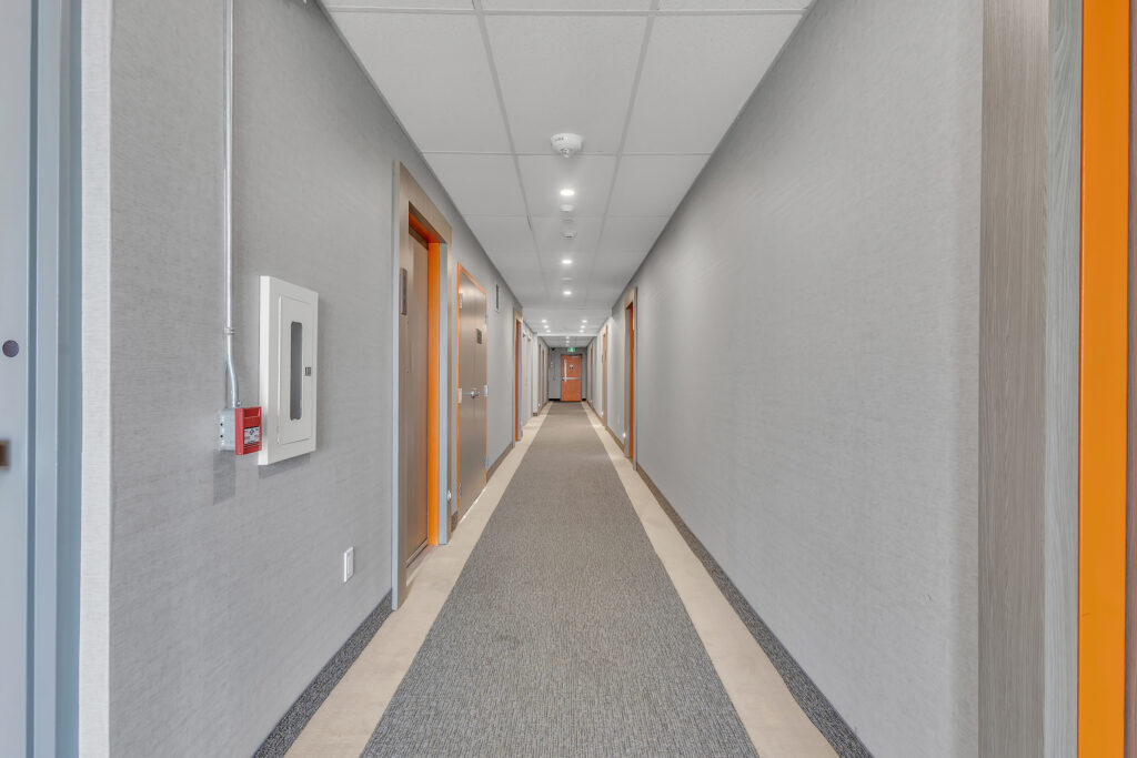 A hallway featuring orange and gray walls, leading to a closed door at the end.