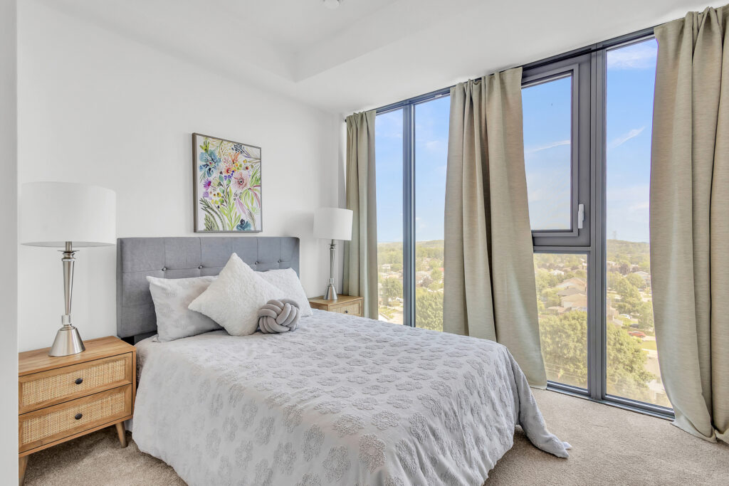 A cozy bedroom featuring a large window with a view of the city skyline.