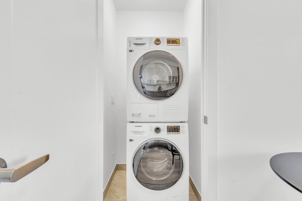 A compact washer and dryer set in a small laundry room with shelves above.