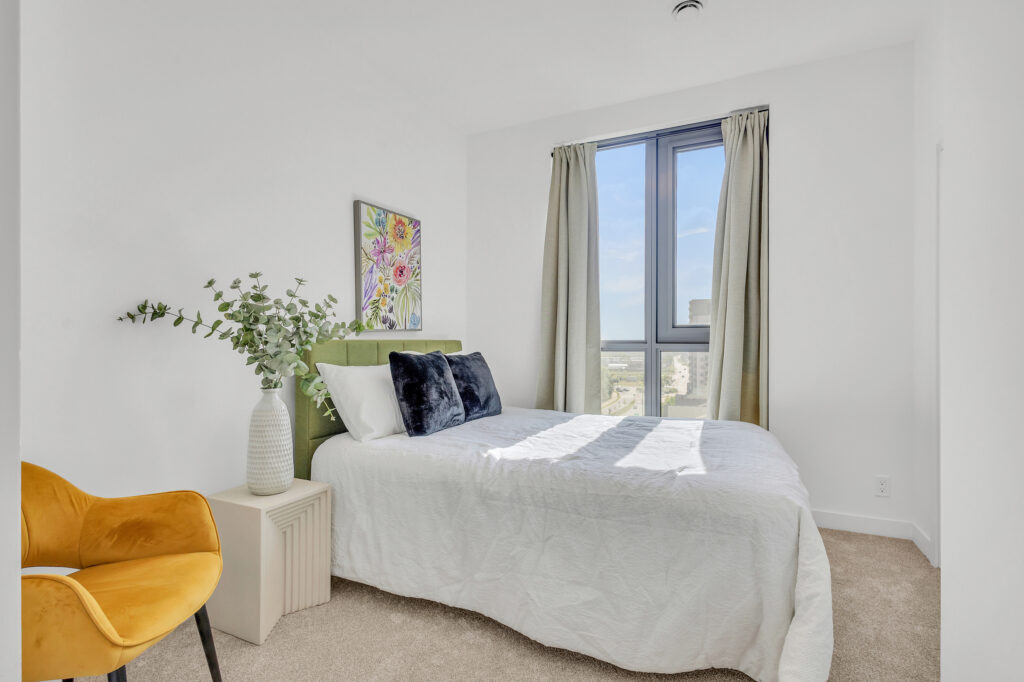 A cozy bedroom featuring a bed, a chair, and a window letting in natural light.
