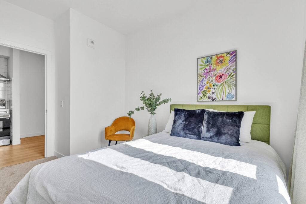 A cozy bedroom featuring a bed, a chair, and a colorful painting on the wall.