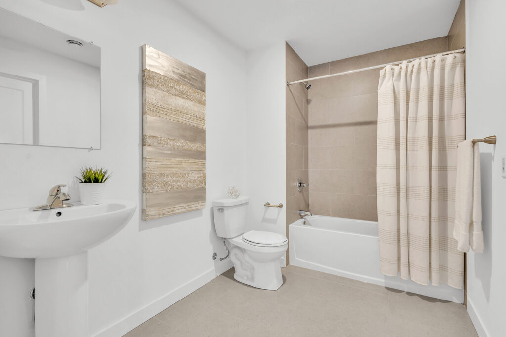 A bathroom featuring a toilet, sink, and shower, with neutral-colored walls and tiled flooring.