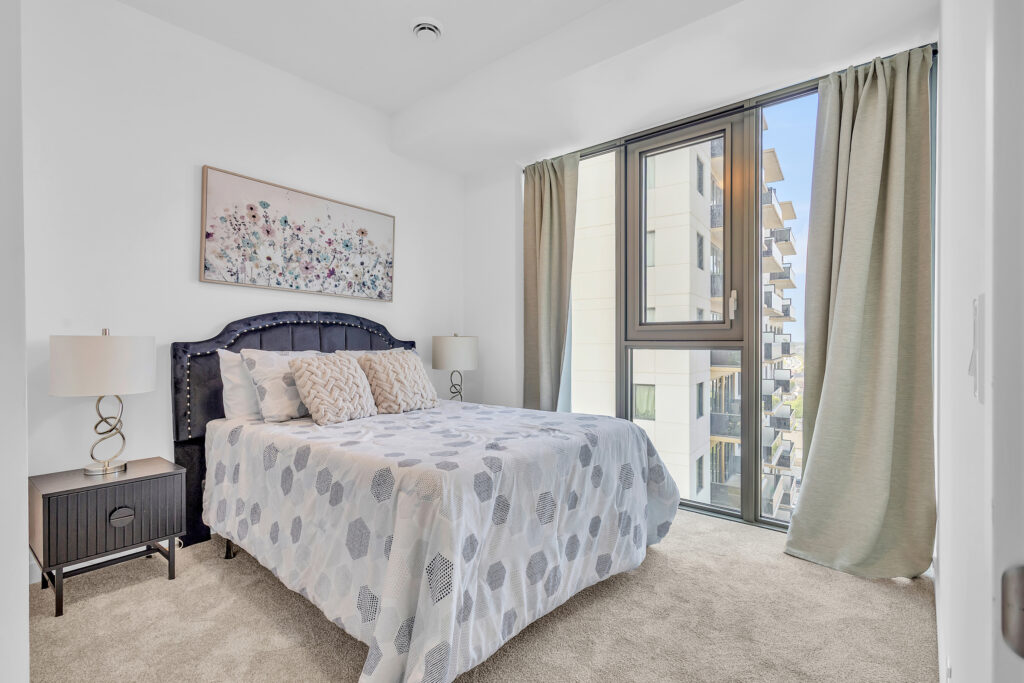 A cozy bedroom featuring a bed, a nightstand, and a window letting in natural light.