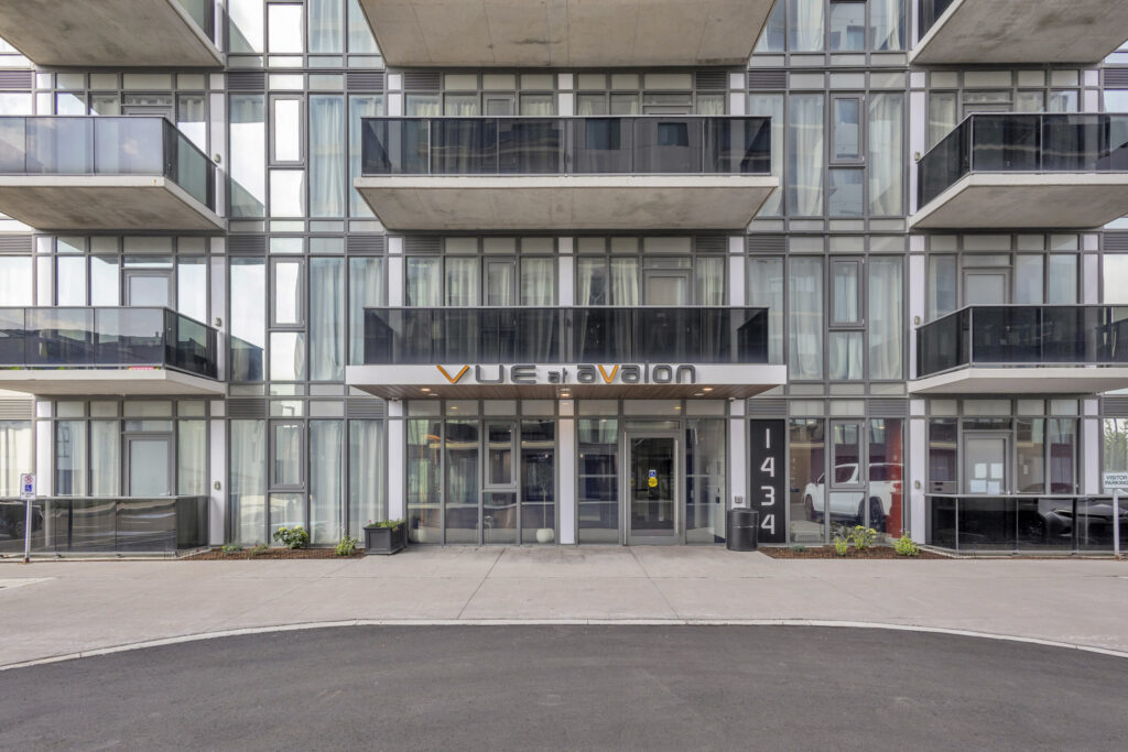 Modern apartment building entrance with glass doors and sleek design, surrounded by greenery.