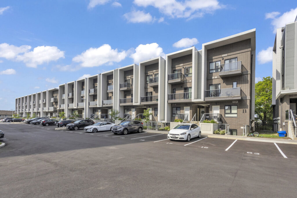 Apartment complex at a street corner with multiple floors and balconies, surrounded by trees and sidewalks.