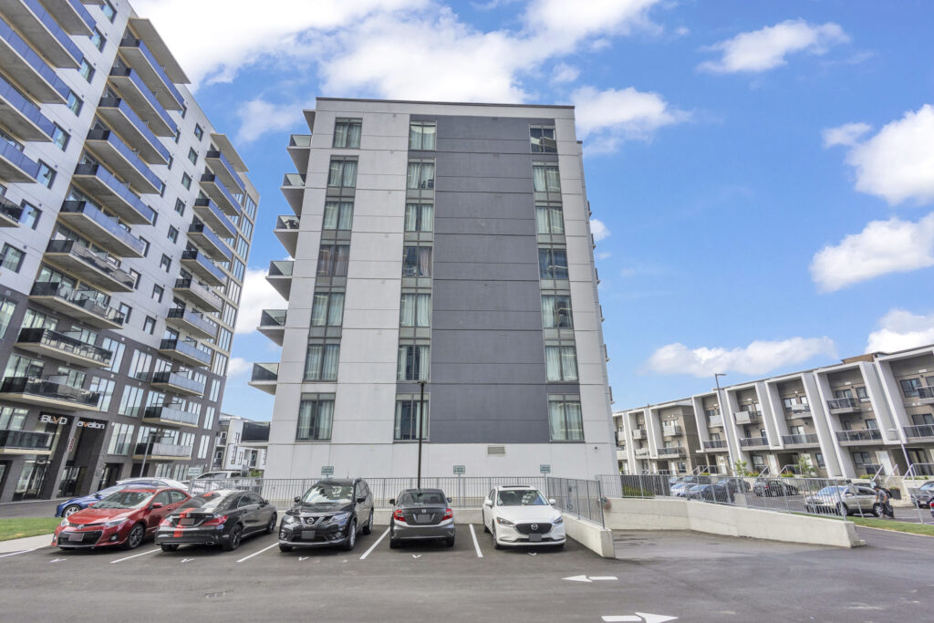 A parking lot filled with cars in front of a tall building under a clear blue sky.