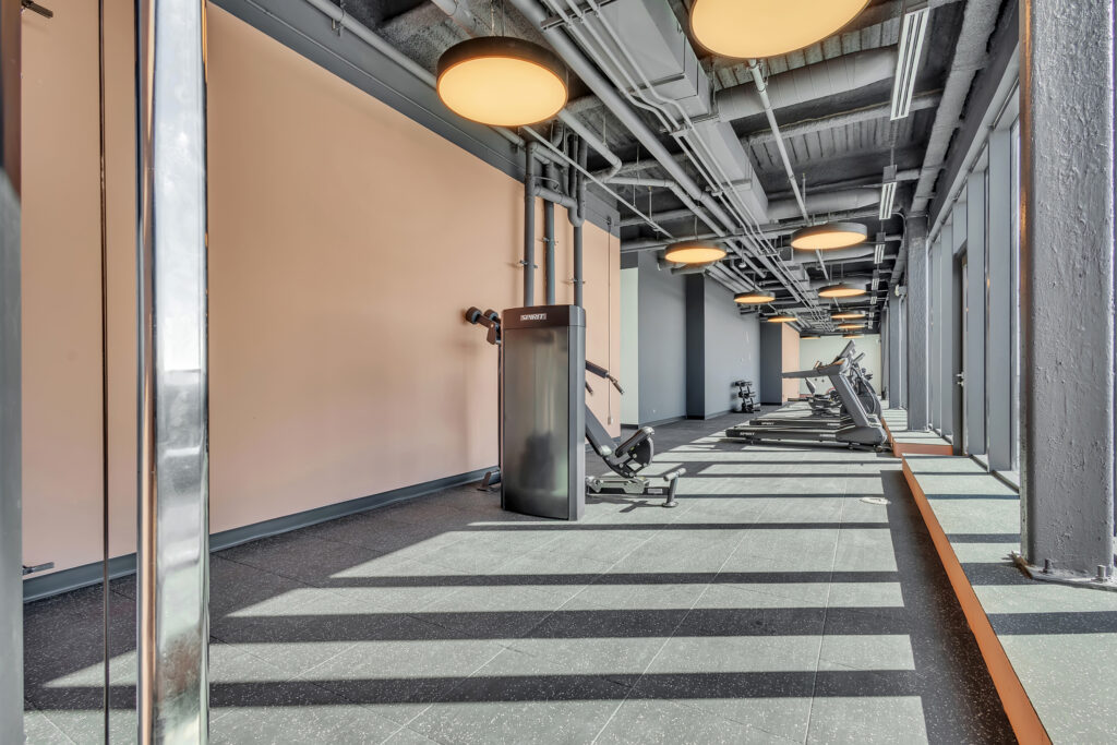 A gym interior featuring a large window and a treadmill positioned near it.
