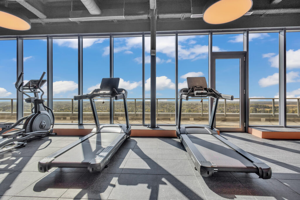 A gym featuring treadmills and large windows with a view of the city skyline.