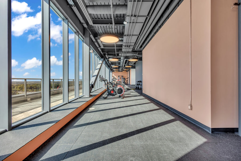 A gym featuring exercise bikes with large windows offering a view of the city skyline.