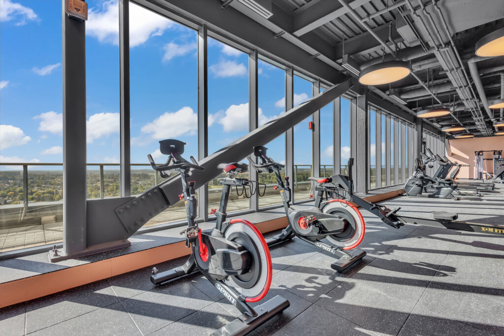 A gym featuring exercise bikes with large windows offering a view of the city skyline.
