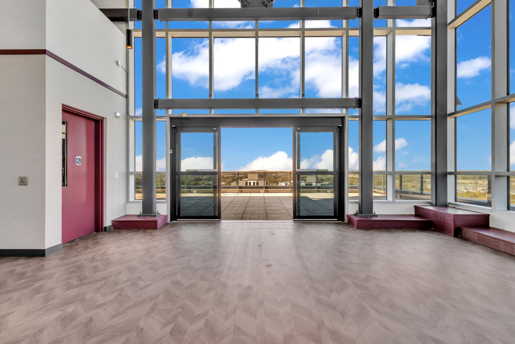 A spacious room with large windows and wooden floors, filled with natural light.