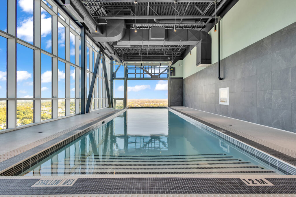 Indoor swimming pool with clear blue water, surrounded by tall windows and a spacious building structure.